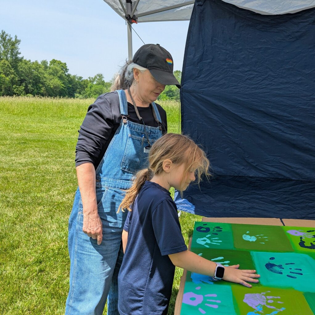 Photo of adult helping a child place a painted hand print on a mural.